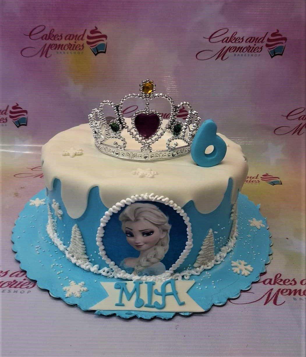 Blue and white Frozen themed Elsa cake with a silver rhinestone tiara, snowflake decorations, and a blue number 6 topper.