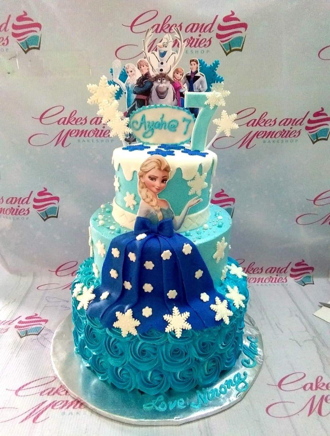 Three-tier Frozen themed cake with Elsa, Anna, and Olaf printouts, blue icing rosettes, and white fondant snowflakes.