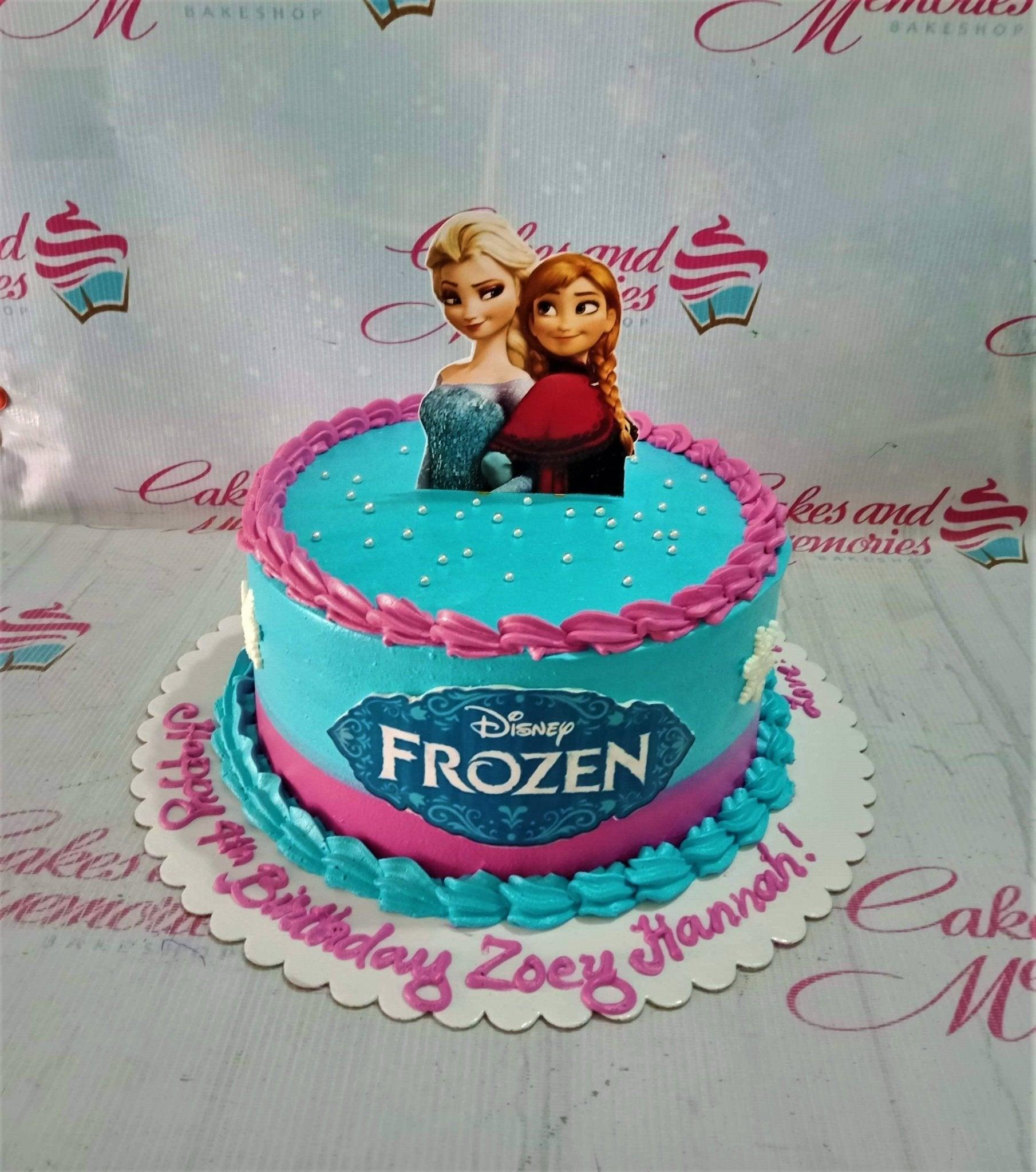 Light blue and pink Frozen themed birthday cake with Elsa and Anna printout topper and snowflake decorations.