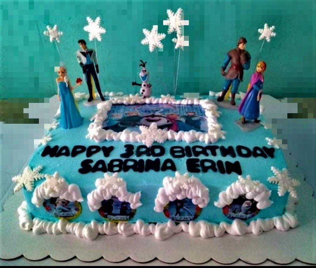Blue Frozen themed rectangle cake with Elsa, Anna, Olaf, and Kristoff toy figurines, snowflake toppers, and edible photo prints.