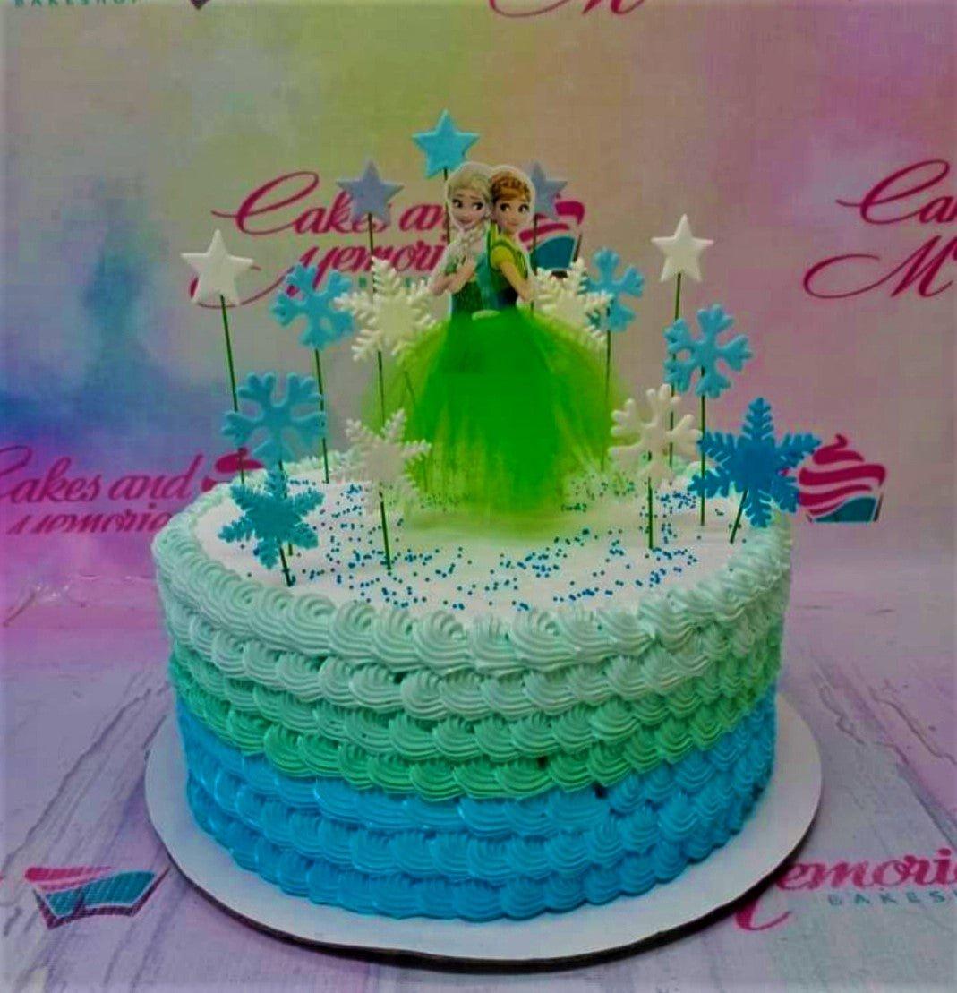 Frozen themed birthday cake with Elsa and Anna printout toppers, blue and green ombre icing ruffles, and snowflake decorations.