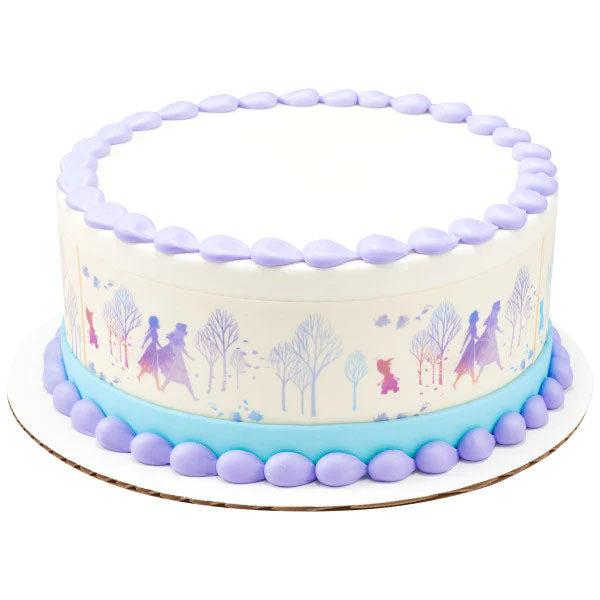 Frozen themed white cake with light blue base border and purple icing dollops featuring a side wrap of Elsa and Anna in a winter forest.
