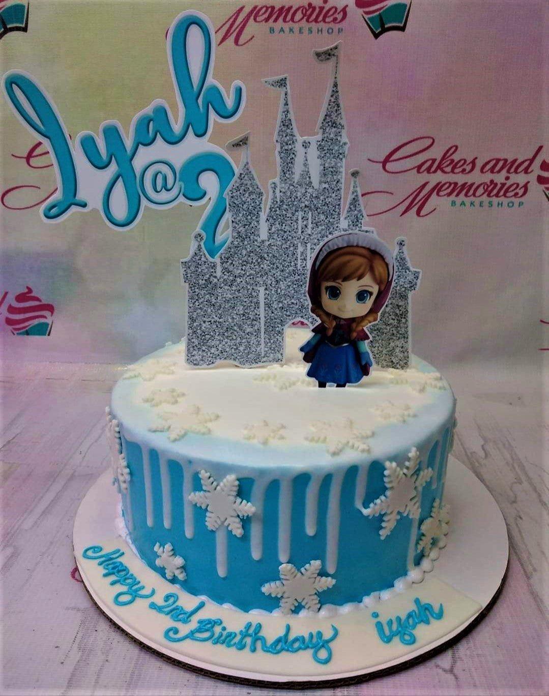Light blue Frozen themed birthday cake with white snowflake decorations, a glittery castle topper, and an Anna character printout.