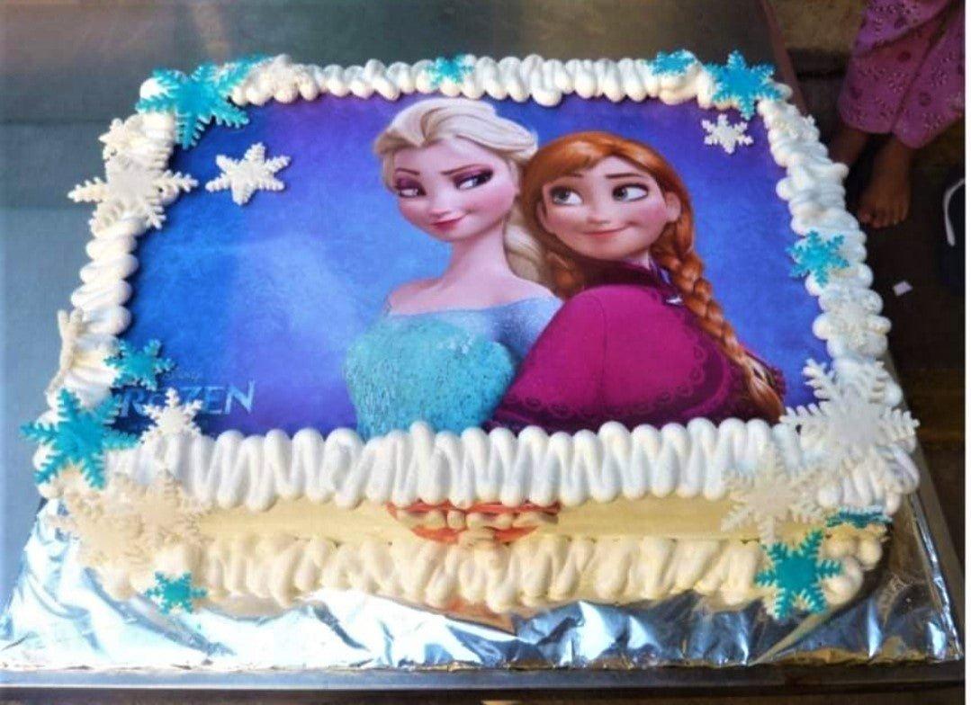 Rectangle Frozen themed cake featuring Elsa and Anna edible photo print with white icing borders and blue and white snowflake decorations.