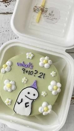 Light green bento cake with white icing flowers and a hand-drawn white character wearing a purple party hat.