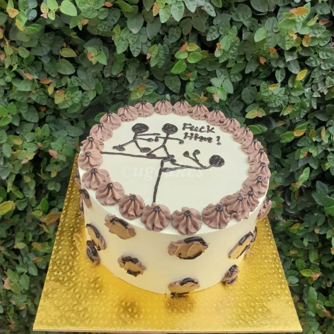 White bento cake with brown piped borders, leopard print sides, and a humorous stick figure drawing on top.