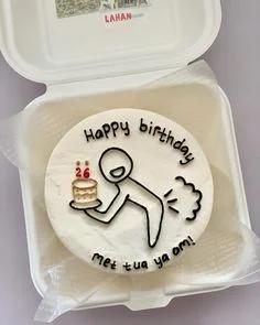 White bento cake with a minimalist black icing doodle of a person holding a small cake and a humorous fart cloud design.