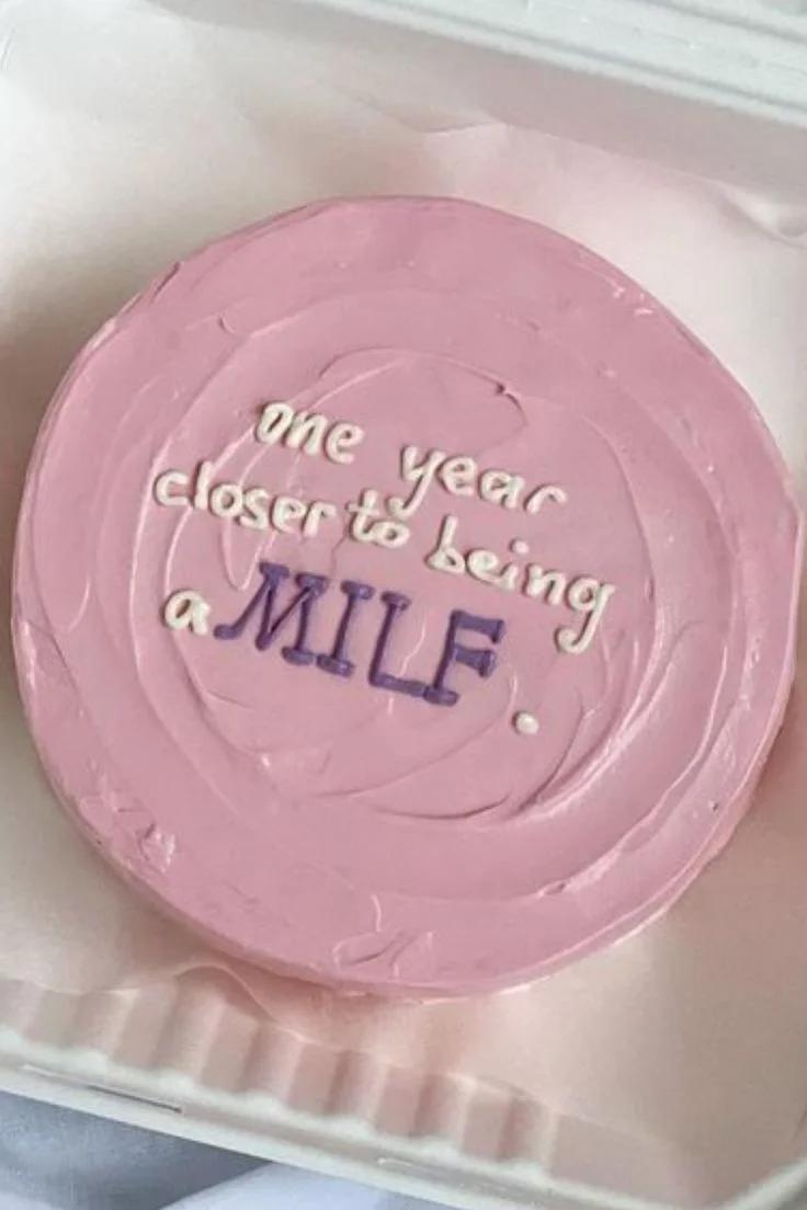 Pink bento cake with textured soft icing and a humorous purple and white message.