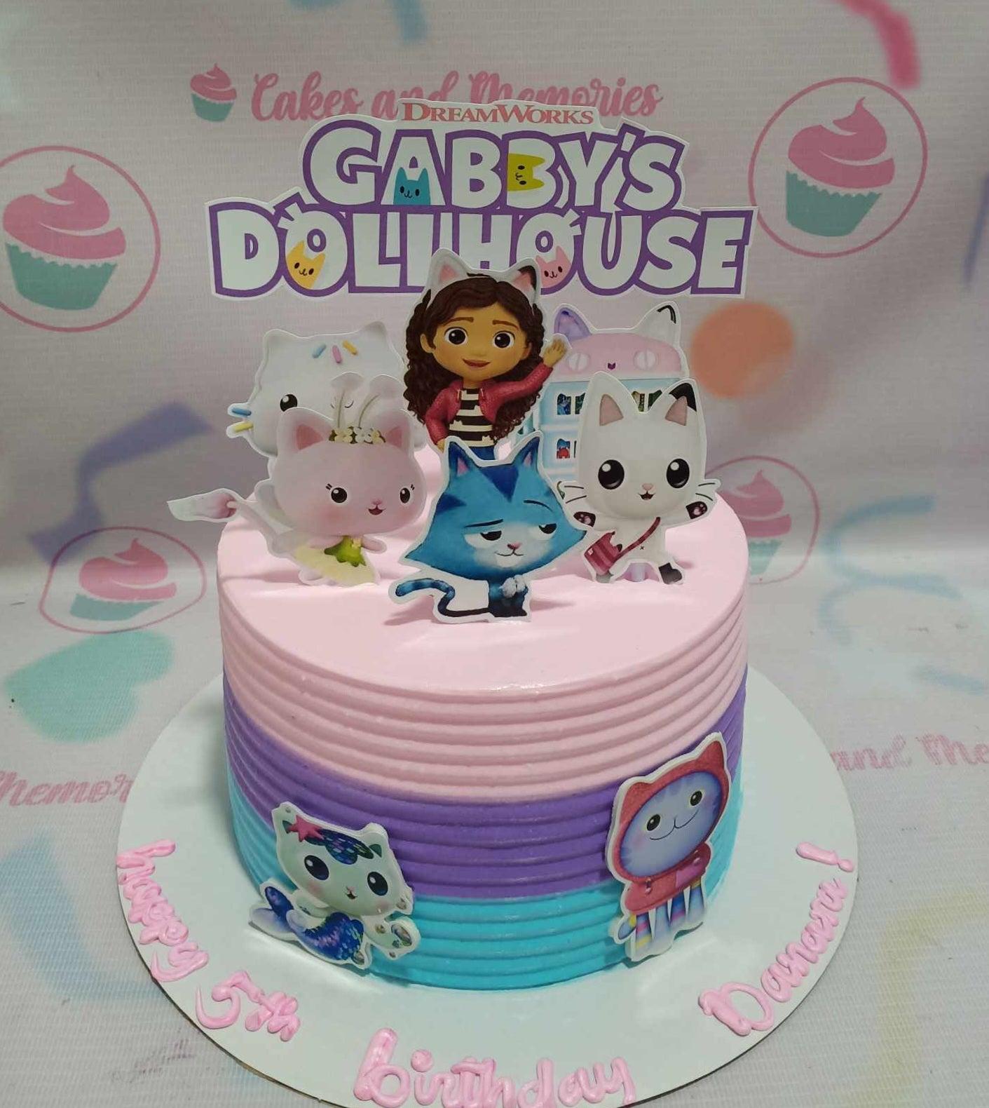 Gabby's Dollhouse themed birthday cake with pink, purple, and light blue horizontal icing ridges and character printouts.