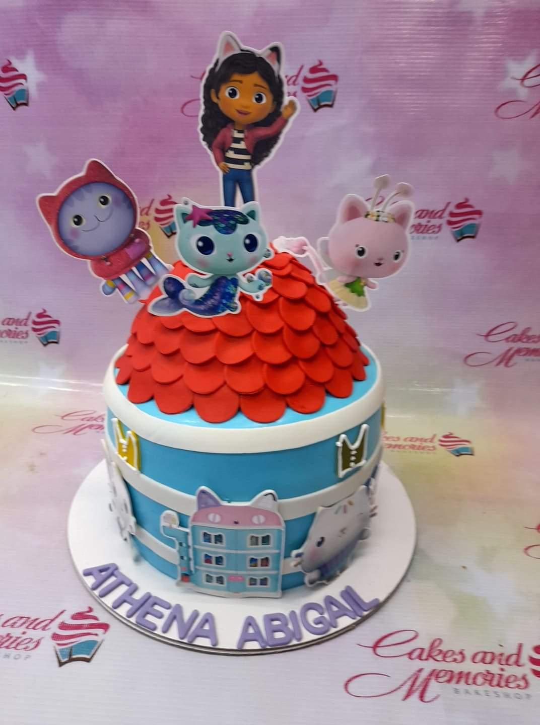 Gabby's Dollhouse themed blue fondant cake with red scale roof and character printouts