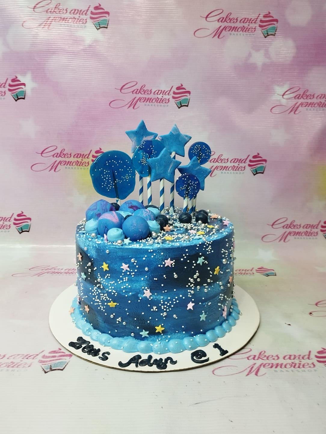 Blue galaxy themed birthday cake with star and moon toppers, silver dragees, and blue fondant spheres.