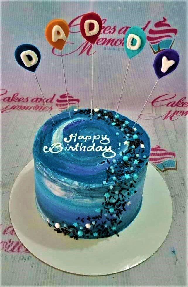 Blue galaxy themed birthday cake for dad with colorful balloon toppers and black sprinkles