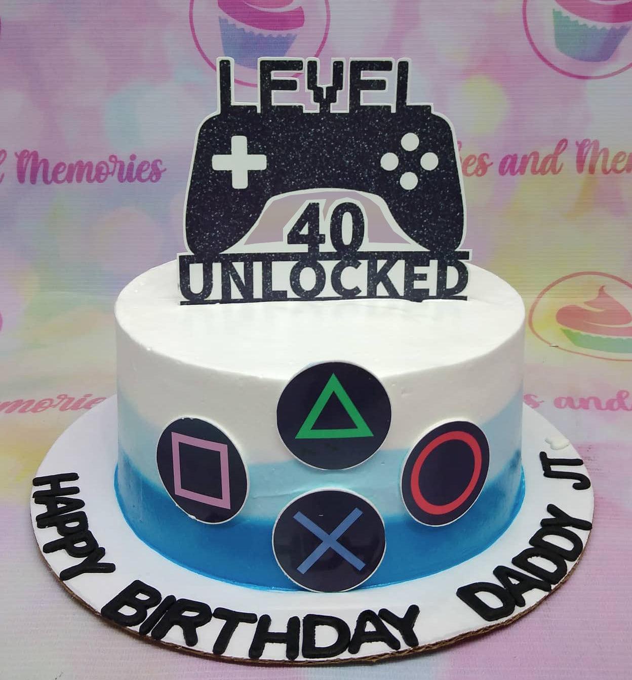 Blue and white gradient gamer birthday cake with a large Level 40 Unlocked controller topper and PlayStation button icons.