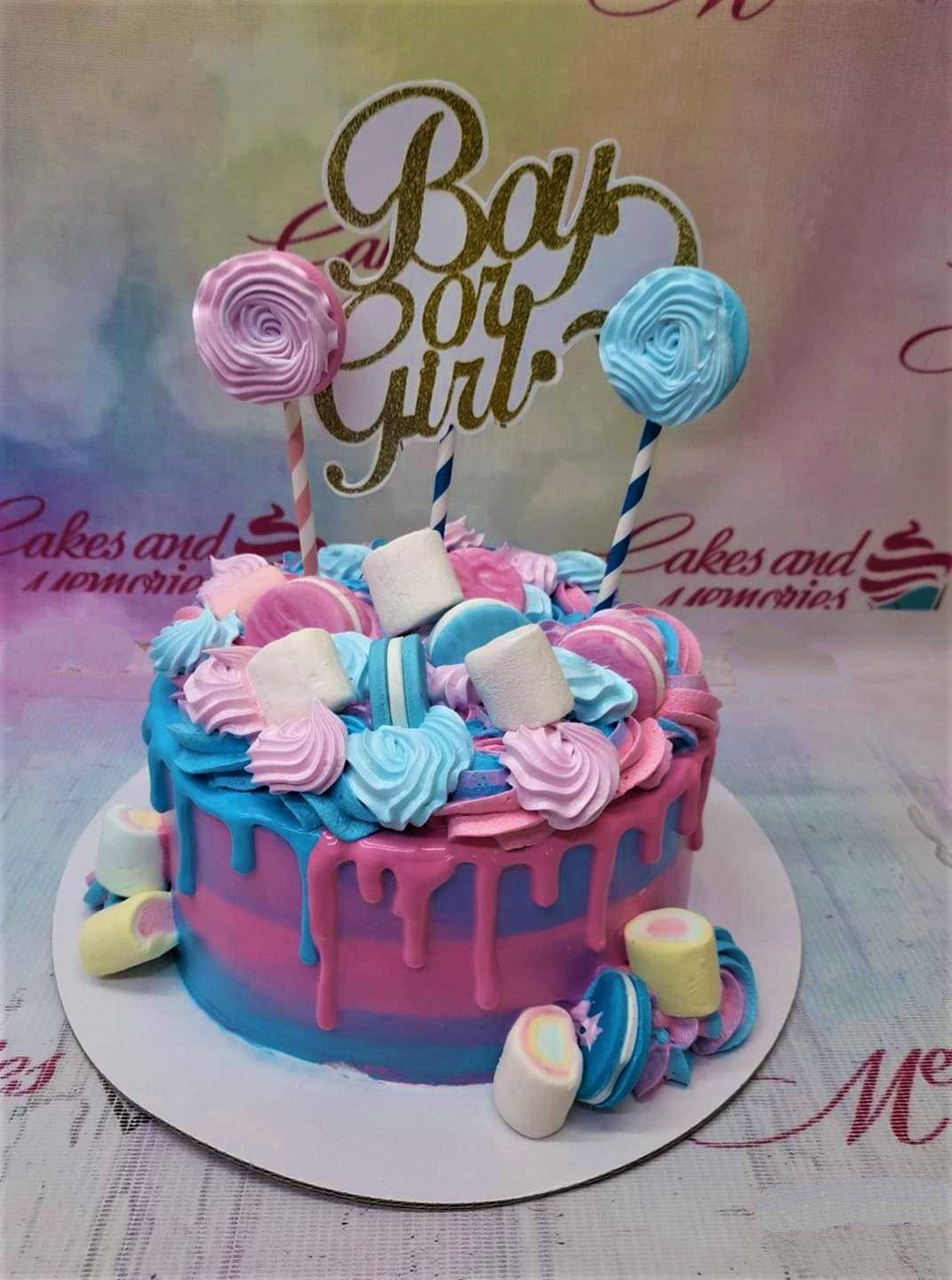 Gender reveal cake with pink and blue gradient icing, drips, meringue pops, marshmallows, and a gold glitter Boy or Girl topper.