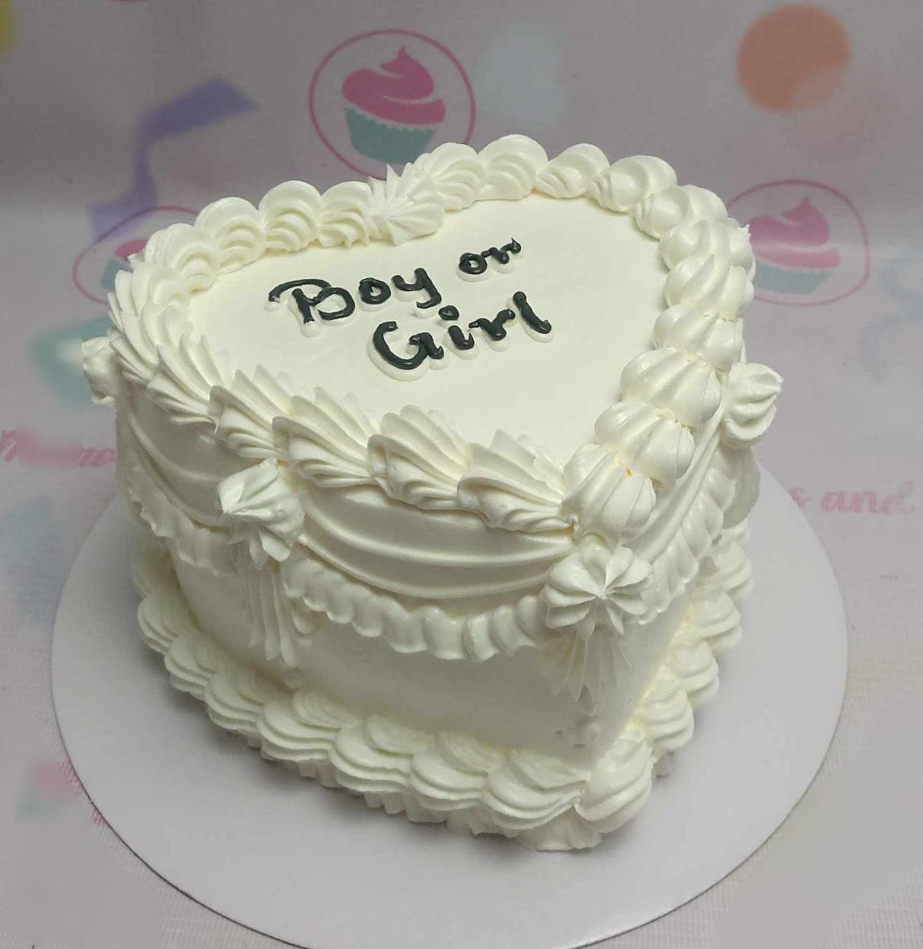White heart-shaped bento cake with vintage-style piped icing ruffles and 'Boy or Girl' message for a gender reveal.