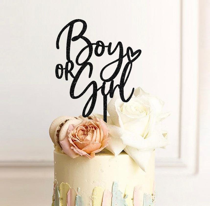 Elegant gender reveal cake with a black glitter Boy or Girl topper, fresh white and peach roses, and pastel palette knife icing strokes.