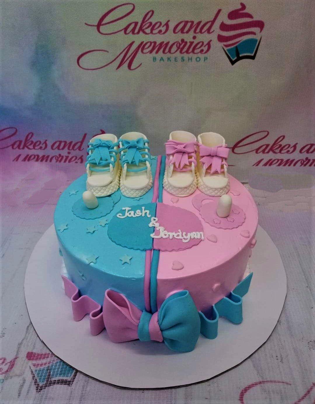 Gender reveal cake split in blue and pink with fondant baby shoes, pacifiers, and a large bow at the base.