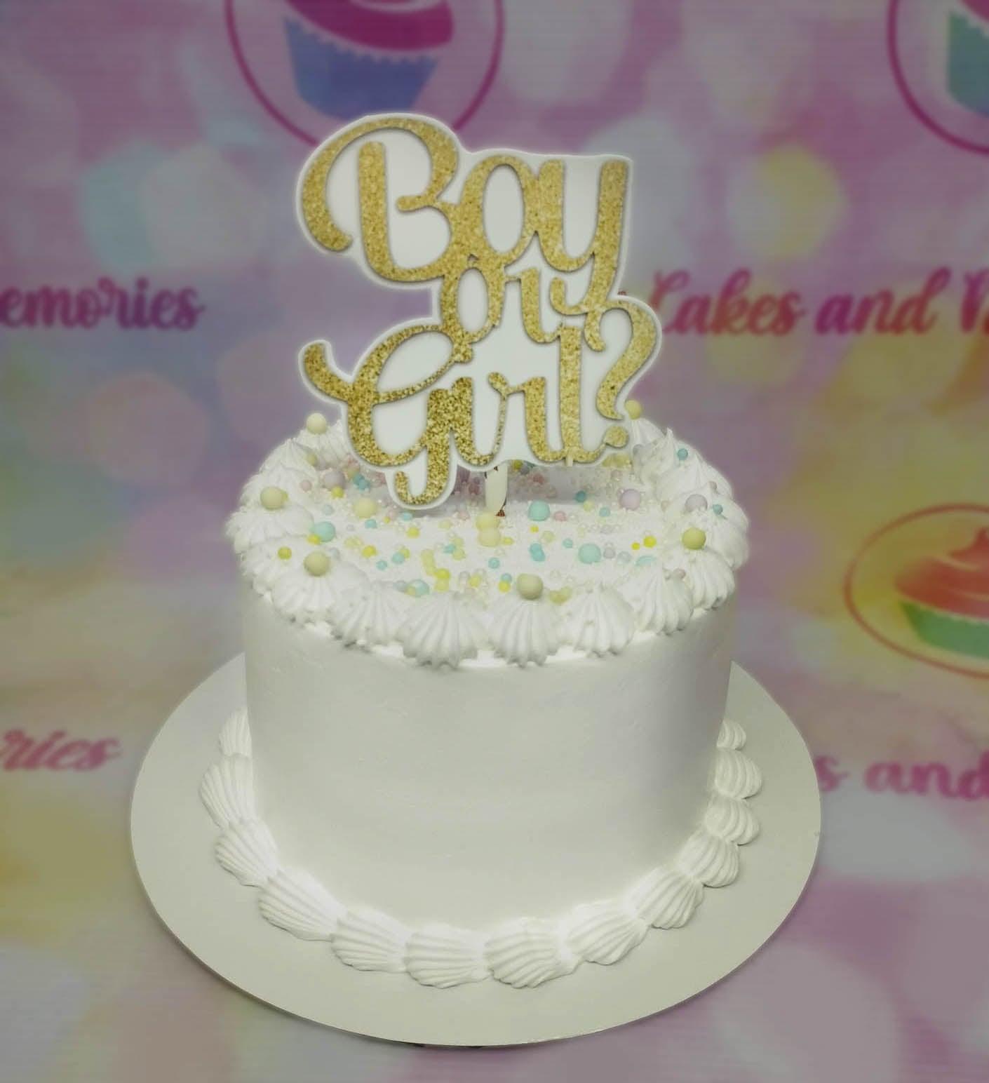 White minimalist gender reveal cake with gold glitter Boy or Girl topper and pastel sprinkles