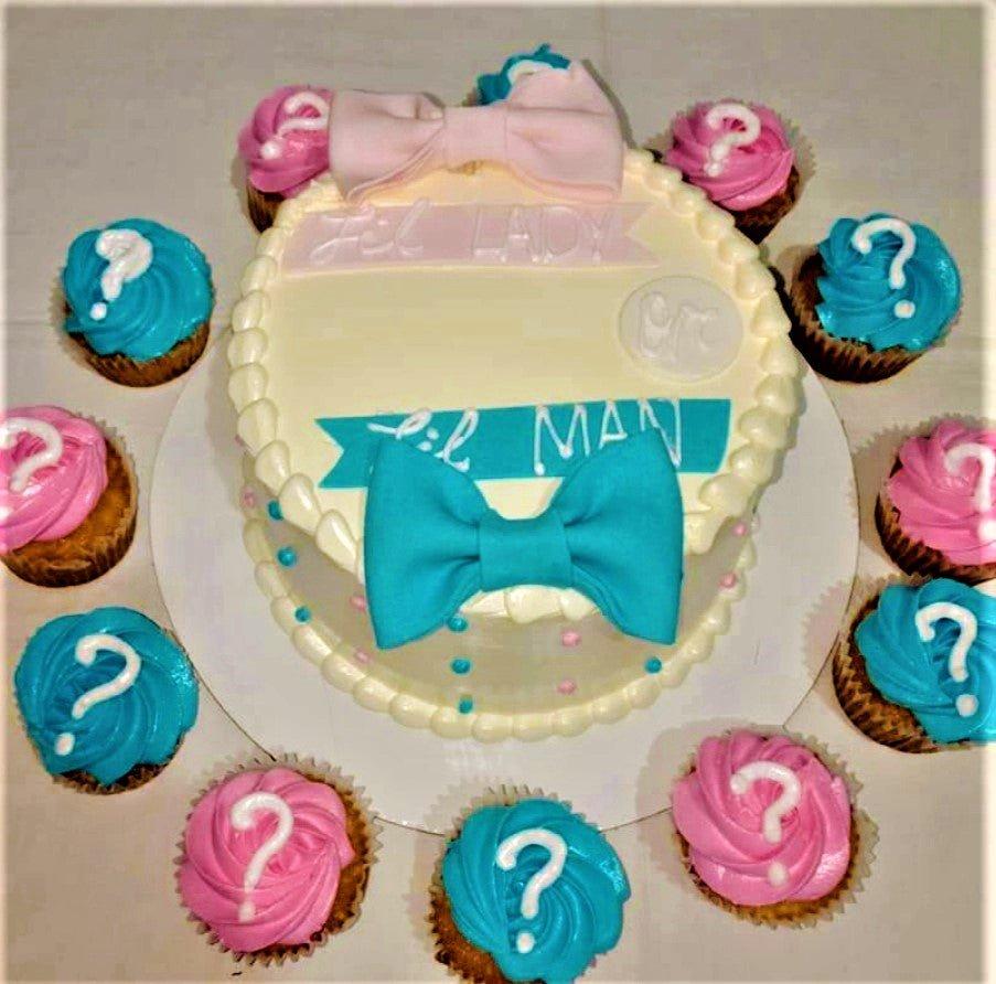 Gender reveal cake with pink and blue fondant bows and matching cupcakes with question marks.