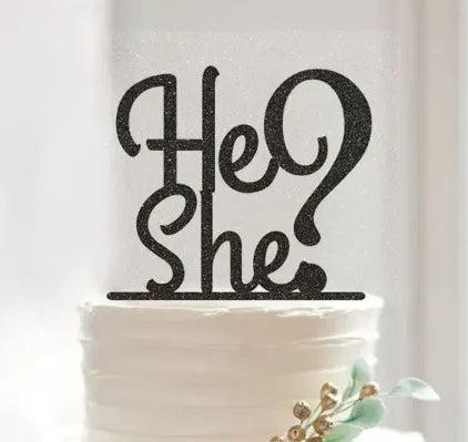 White minimalist gender reveal cake with a black glittery He or She question mark topper and gold floral accents.