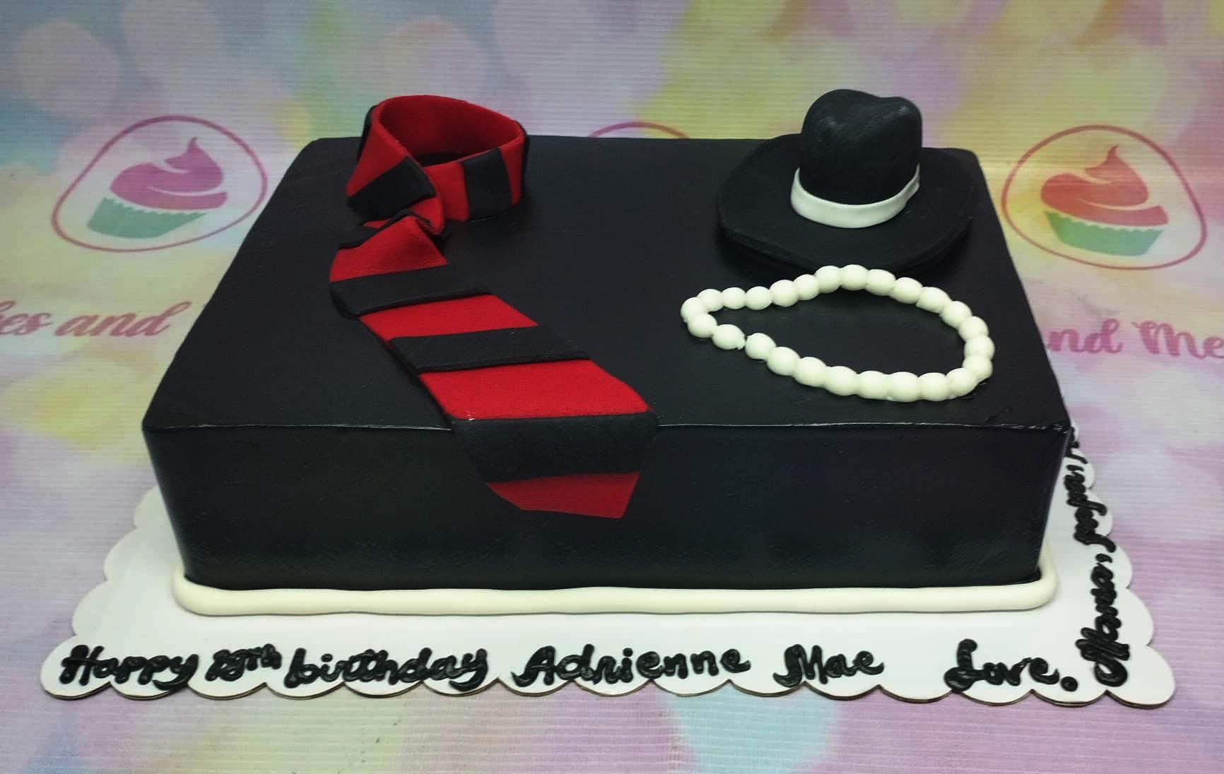 Black rectangle fondant cake with a red and black striped tie, a black fedora hat, and a white pearl necklace topper.