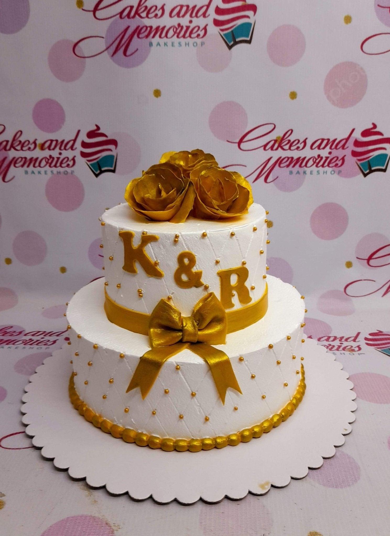 Elegant 2-tier white quilted cake with gold roses, a large gold bow, and gold initials K and R.