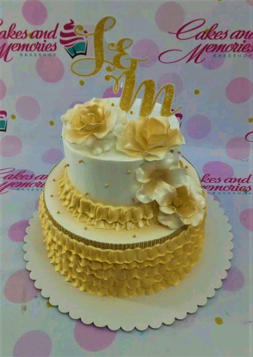 Elegant two-tier white and gold cake with ruffled icing and large edible gold roses on a white scalloped base.