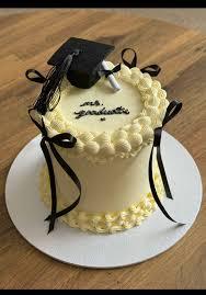 Elegant white graduation cake with a black graduation cap topper, a small diploma, and black ribbon bows around the sides.
