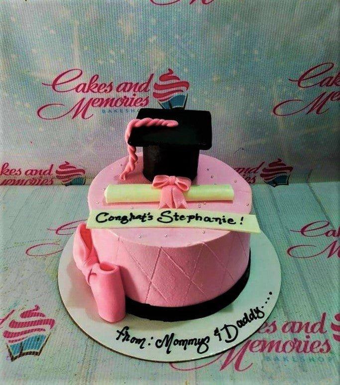 Pink graduation cake with a black fondant graduation cap, a white diploma with a pink bow, and a message for Stephanie.