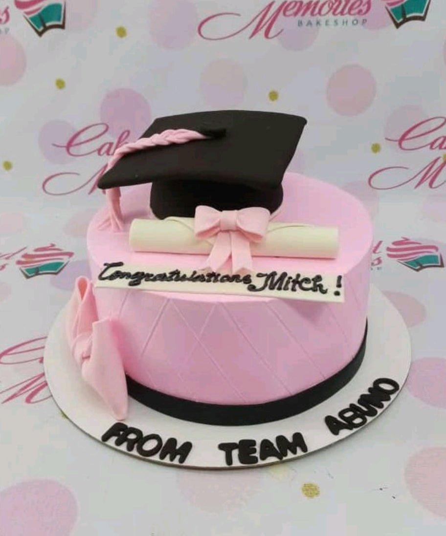 Pink graduation cake with a black fondant graduation cap, a white diploma with a pink bow, and a quilted icing pattern.