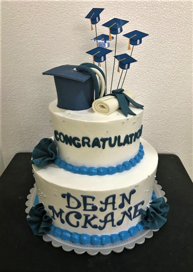 White 2-tier graduation cake with navy blue graduation cap, diploma, and blue icing borders.