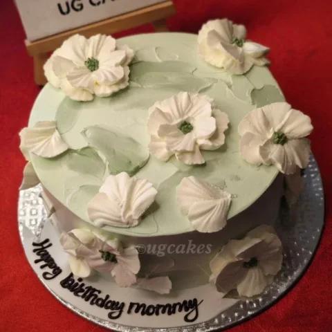 Light green minimalist cake with white palette knife icing flowers and a birthday message on the base board.