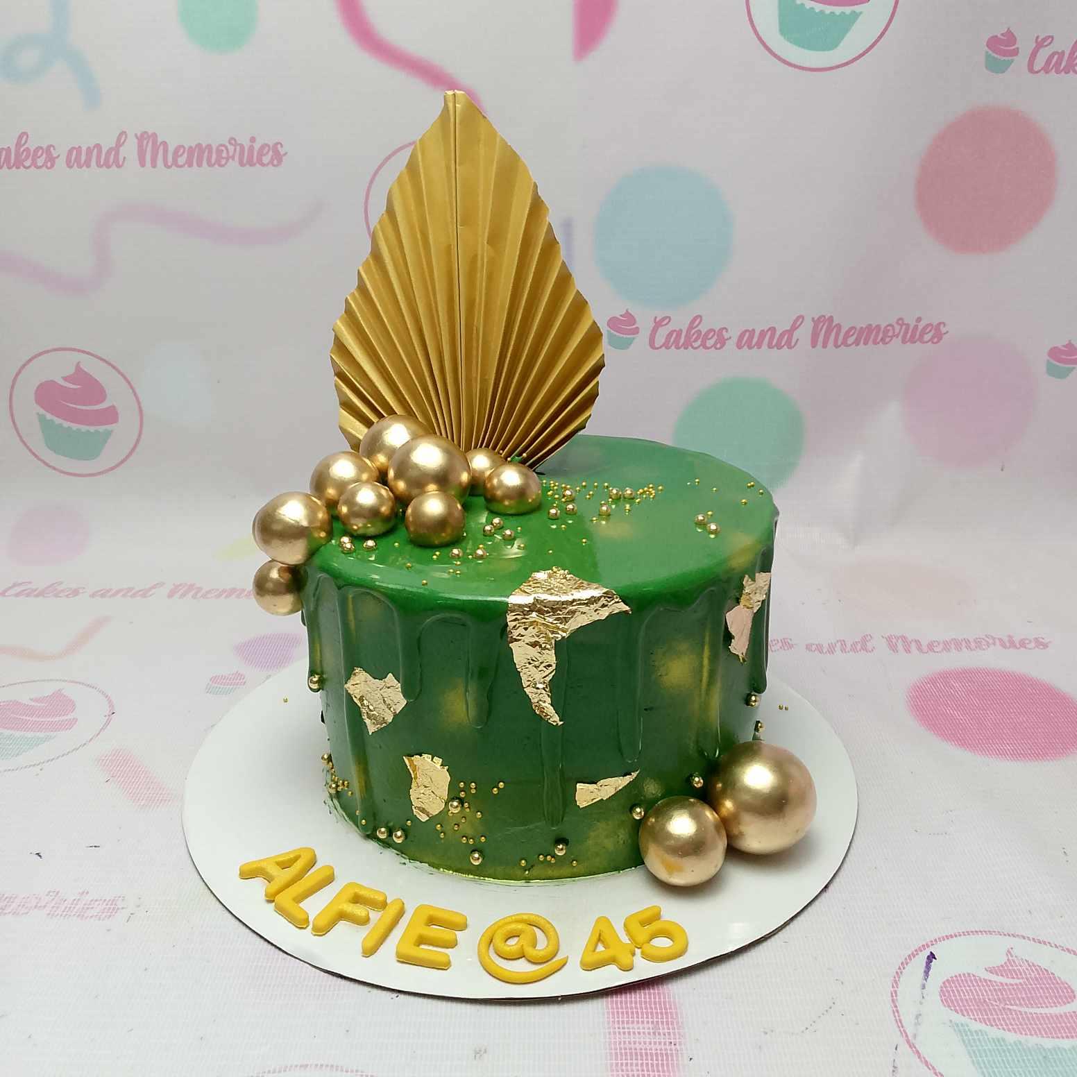 Green 1-tier birthday cake with gold drip, gold leaf accents, gold spheres, and a large gold fan topper.