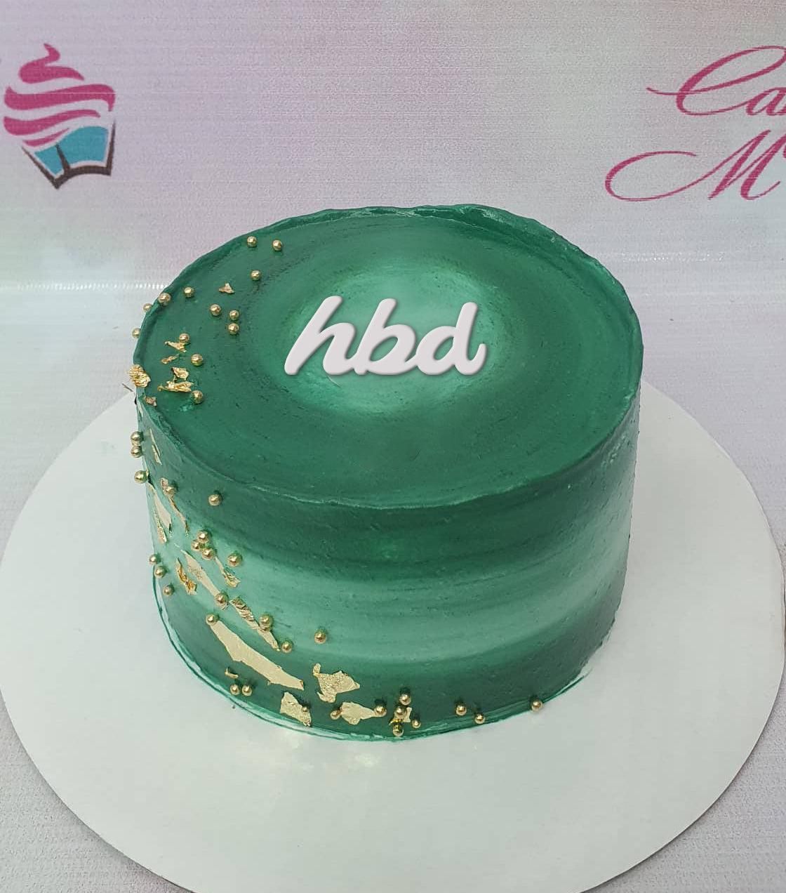 Minimalist dark green bento cake with a white hbd message, gold leaf accents, and gold pearl sprinkles.