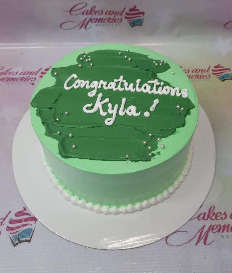Light green minimalist cake with a dark green palette knife icing stroke on top and silver dragees.