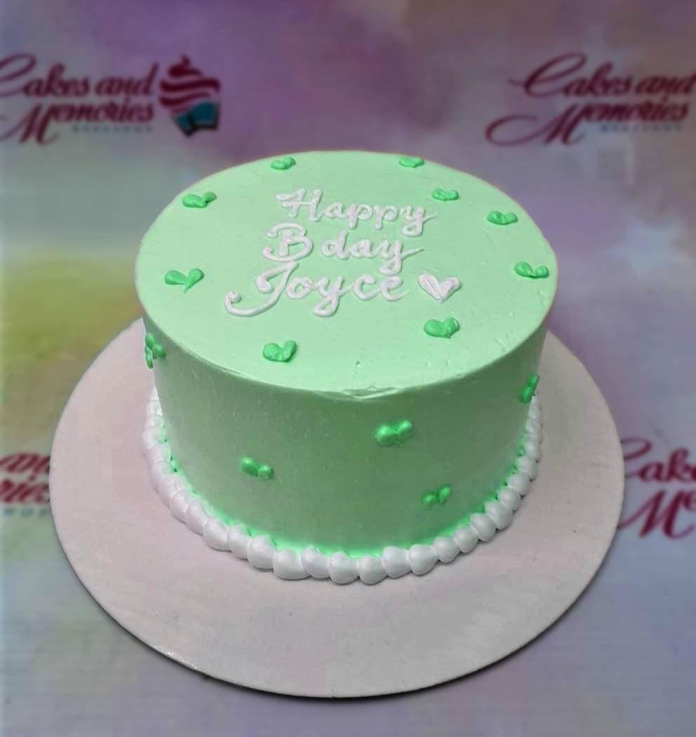 Light green minimalist bento cake with white piped icing message and small green heart decorations.