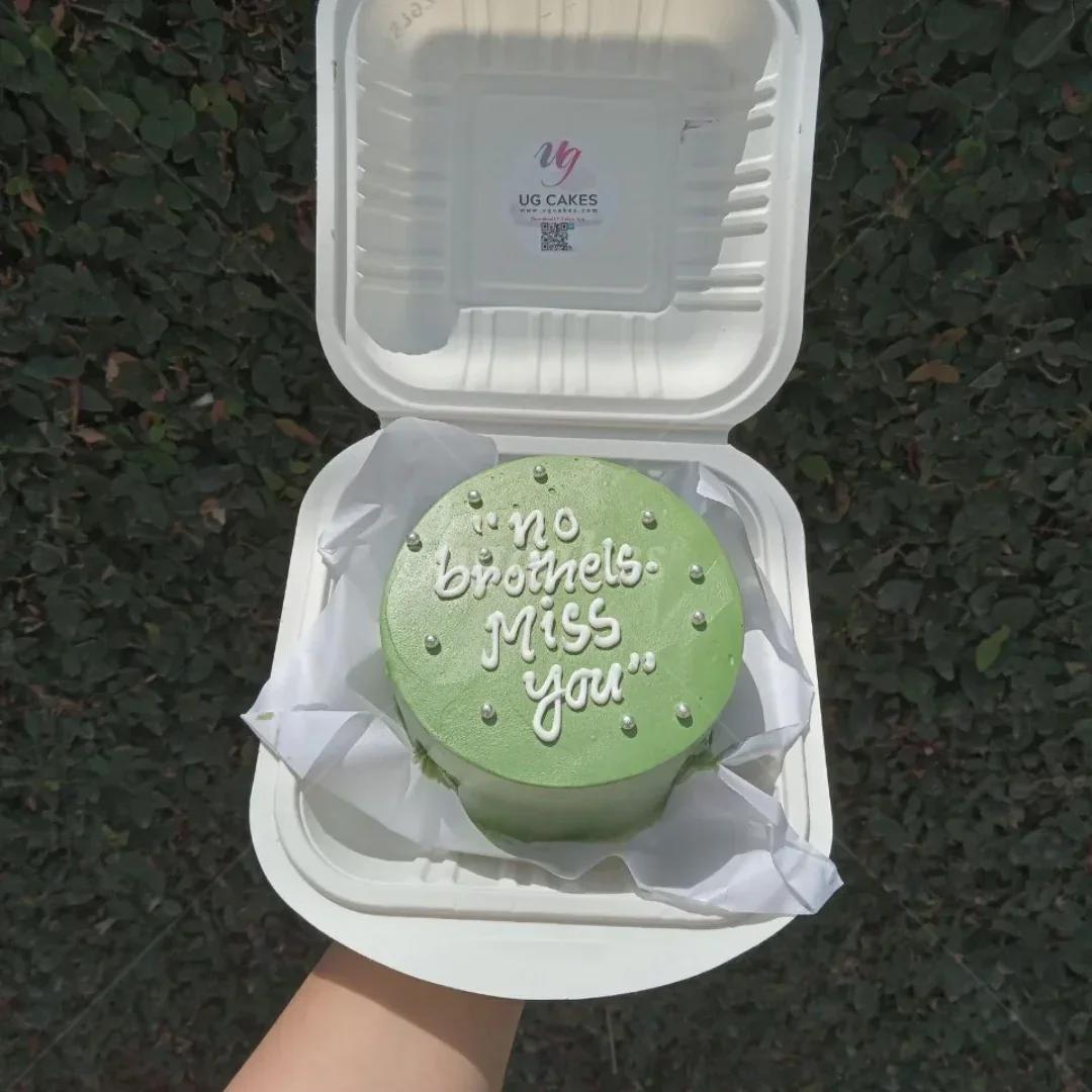 Green bento cake with white icing text and silver dragees in a white container