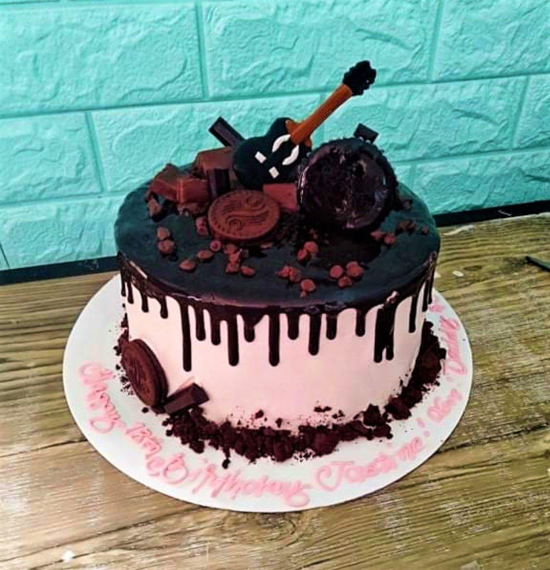 Pink and chocolate drip cake with guitar topper, chocolate bars, and cookies for a 13th birthday celebration.