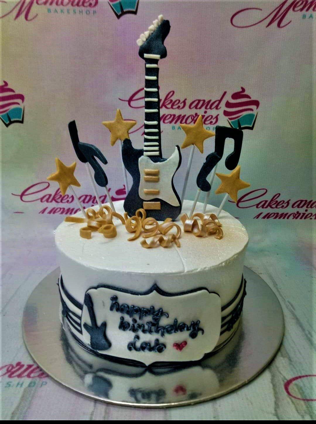 White 1-tier guitar birthday cake with black and gold music notes, stars, and a fondant guitar topper.