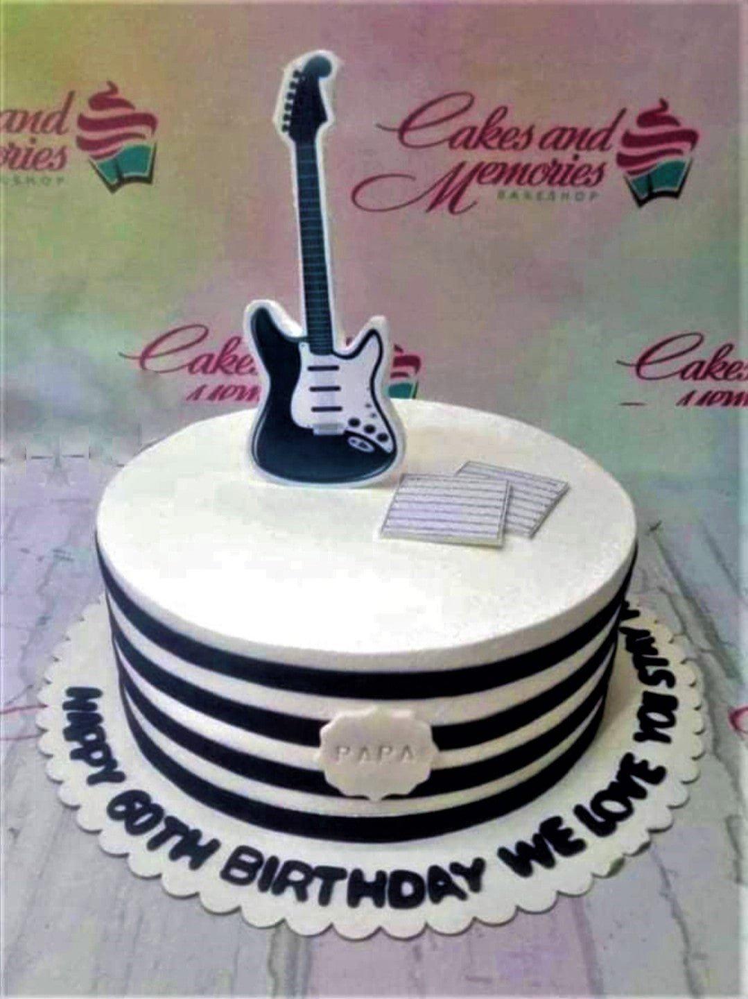 White 1-tier birthday cake with black horizontal stripes, a black and white guitar printout topper, and music sheet accents.