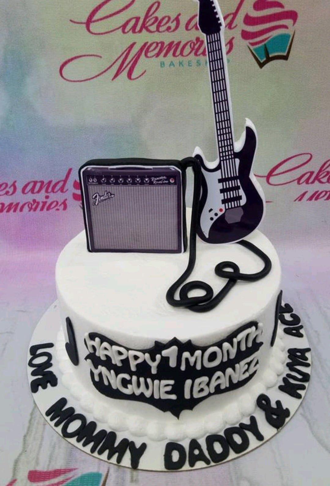 White 1-tier music themed cake featuring a guitar and amplifier printout toppers with black icing text and borders.