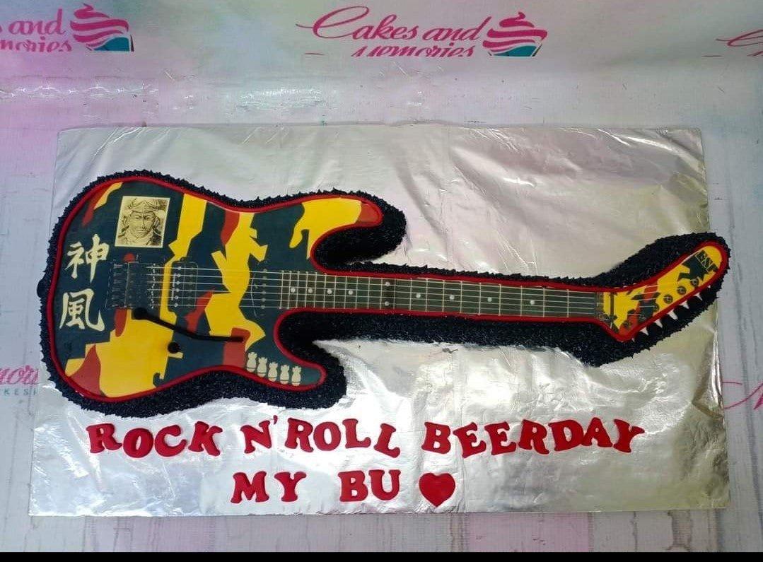 Custom guitar-shaped cake with black textured icing and printed rock and roll graphics on a silver board.