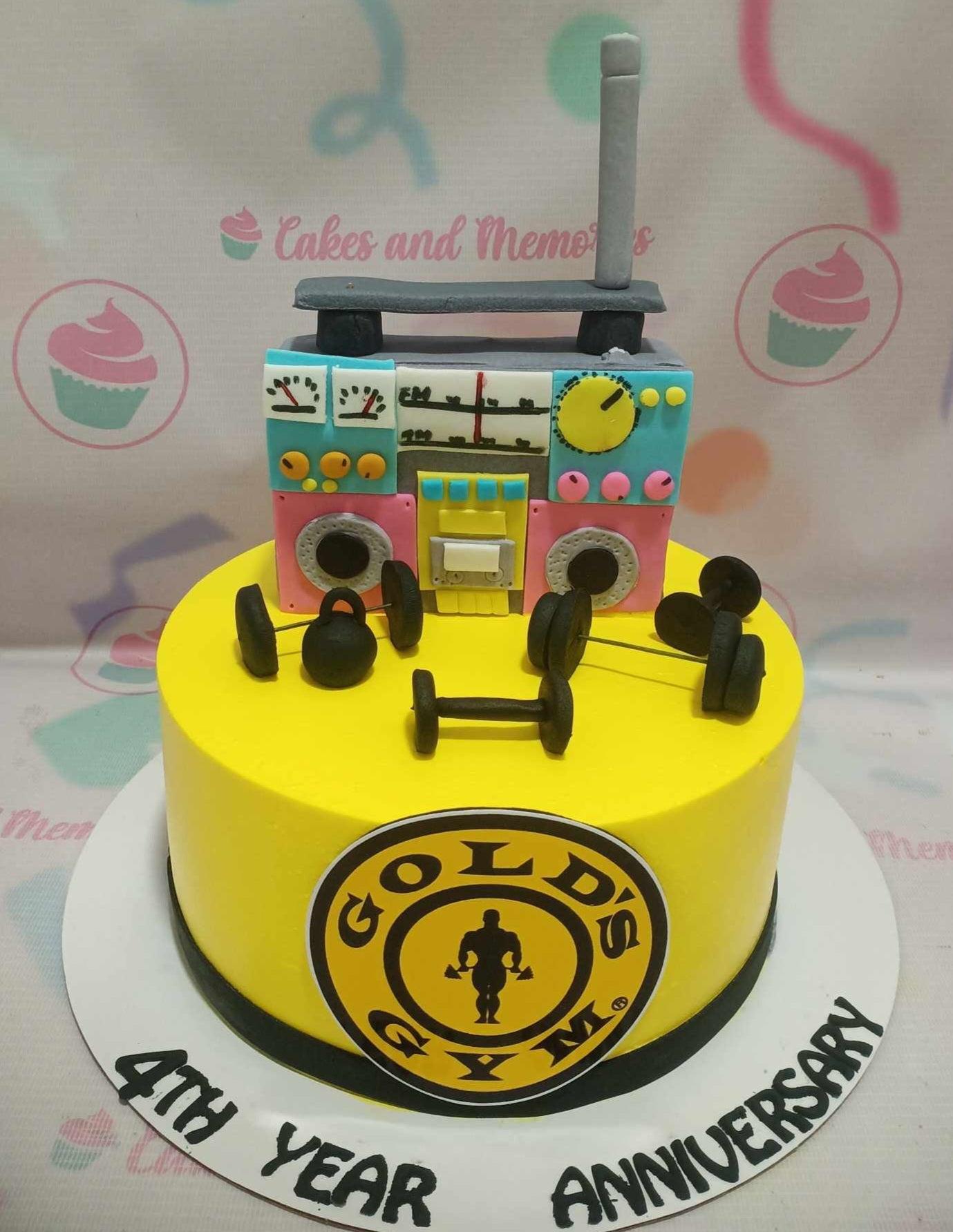 Yellow gym themed cake with a 3D fondant boombox and dumbbells, featuring a Gold's Gym logo and anniversary message.