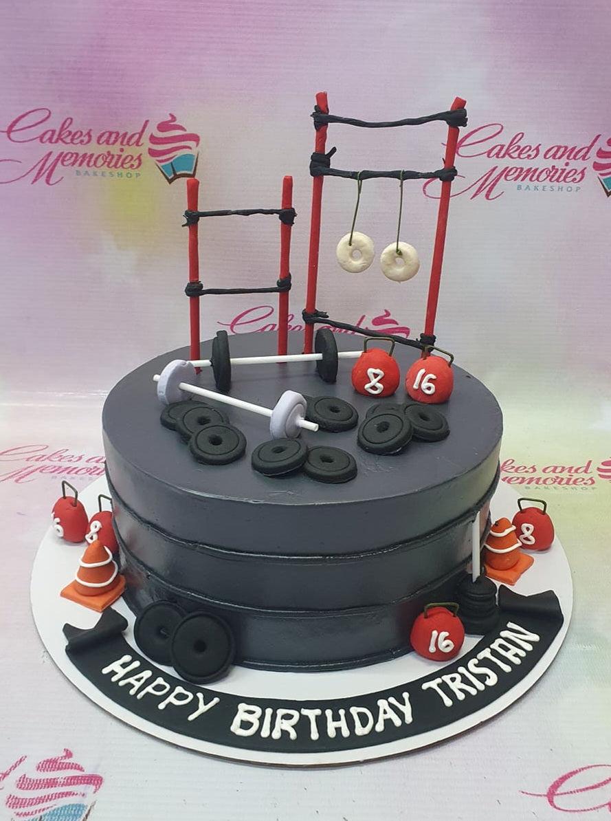 Dark gray gym themed birthday cake with fondant weights, barbells, kettlebells, and a pull-up bar topper.