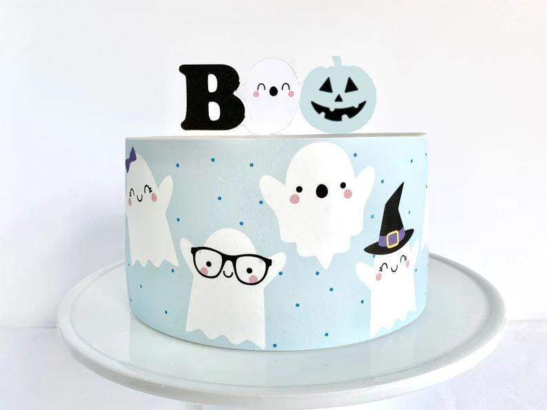 Light blue Halloween ghost cake with cute ghost printouts and a pumpkin topper on a white cake stand.