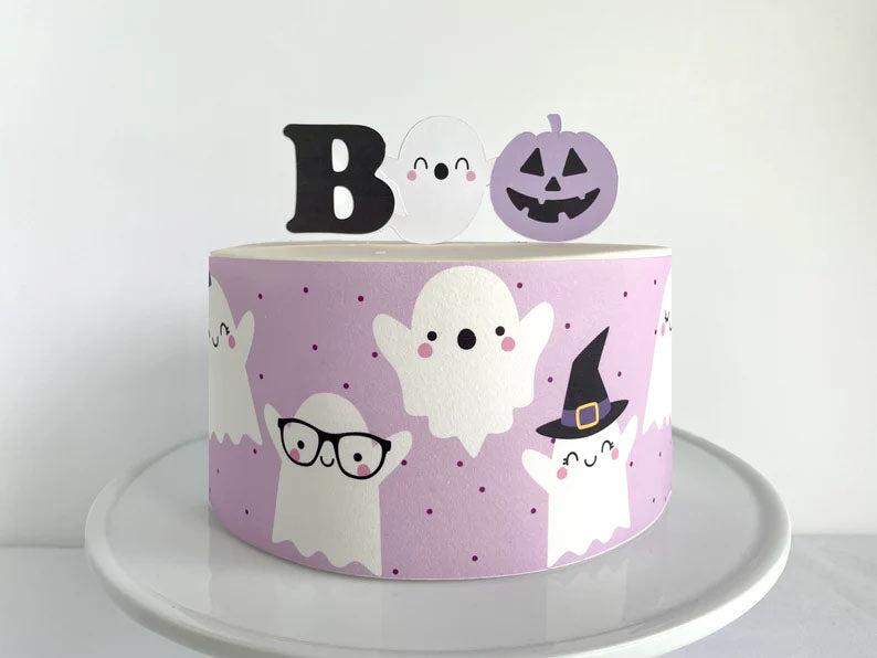 Purple Halloween ghost cake with a wrap-around print of cute ghosts and a BOO topper with a pumpkin.
