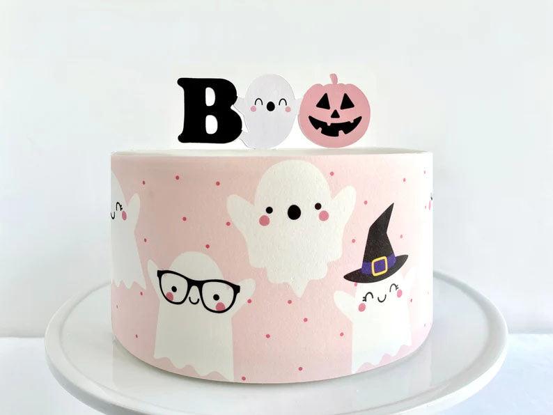 Pink and white Halloween ghost cake with cute ghost printouts and a Boo topper featuring a pumpkin and ghost.