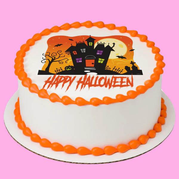 White round Halloween cake with orange icing borders and a haunted house printout topper featuring a full moon and bats.
