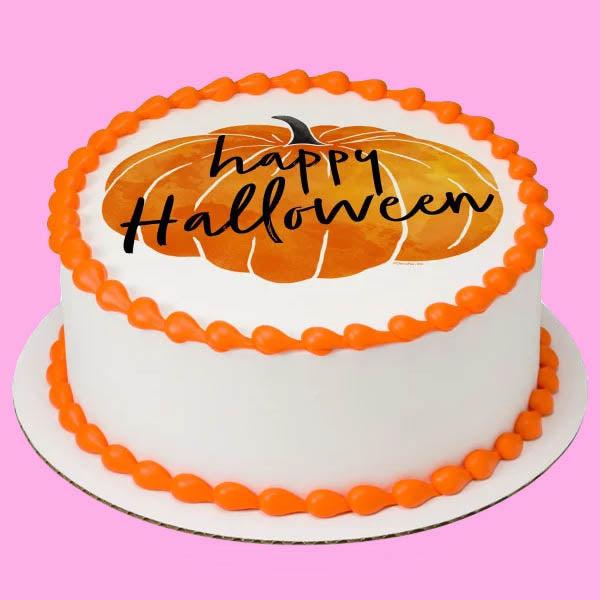 White round Halloween cake with orange piped borders and a large pumpkin printout on top featuring Happy Halloween text.