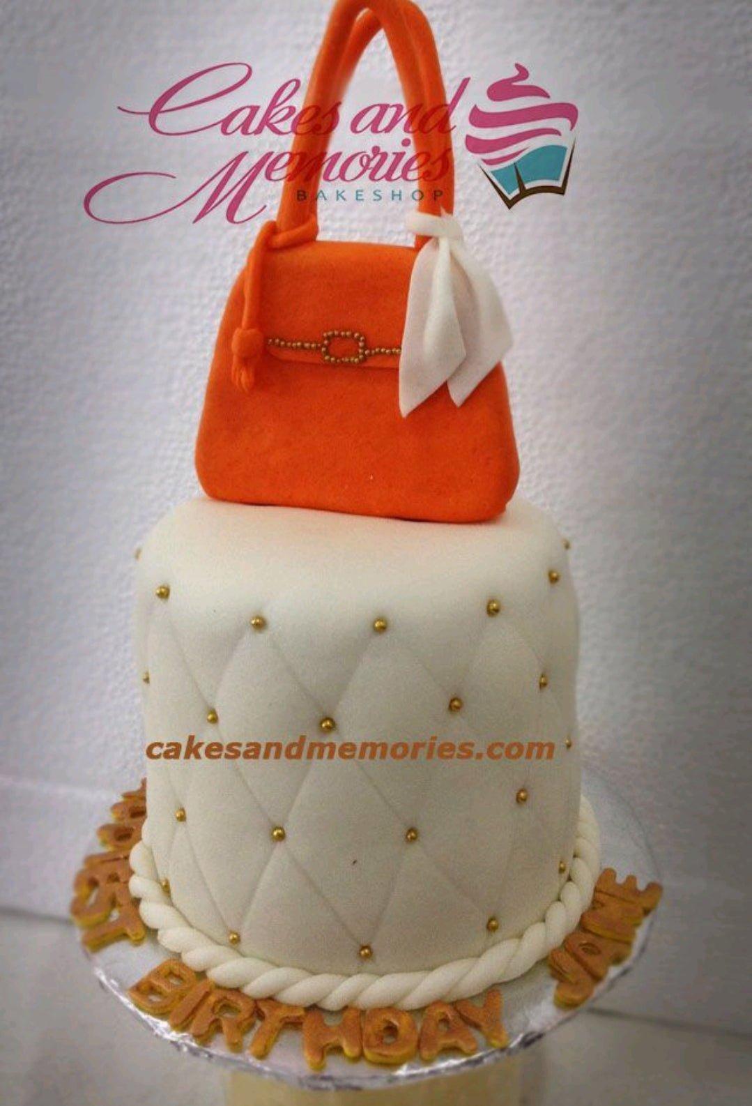White quilted fondant cake with gold dragees and a large orange gumpaste handbag topper.